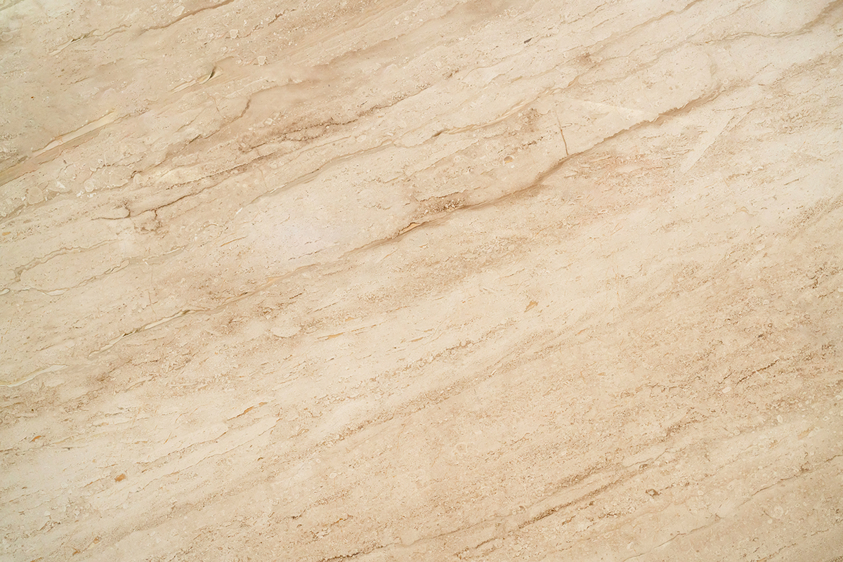 Nahaufnahme einer polierten, beigefarbenen Marmoroberfläche mit ausgeprägter, diagonaler Maserung.