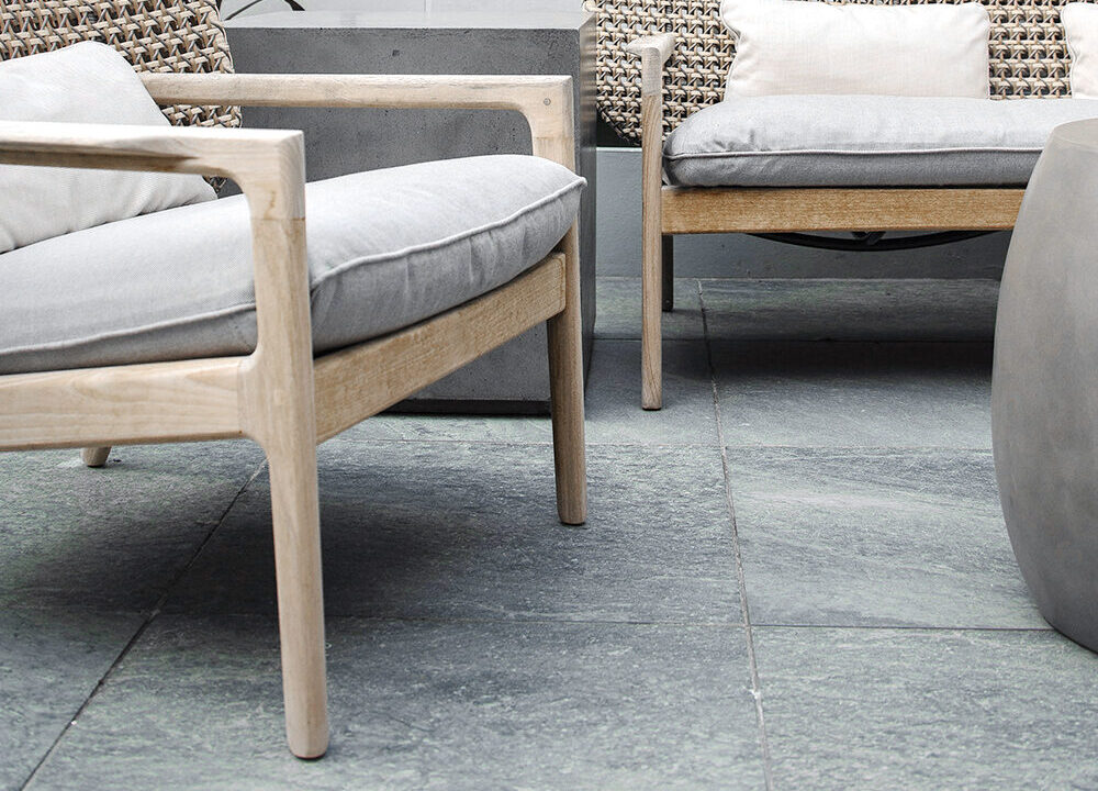 Holz-Sessel mit grauen Kissen auf Steinterrasse.